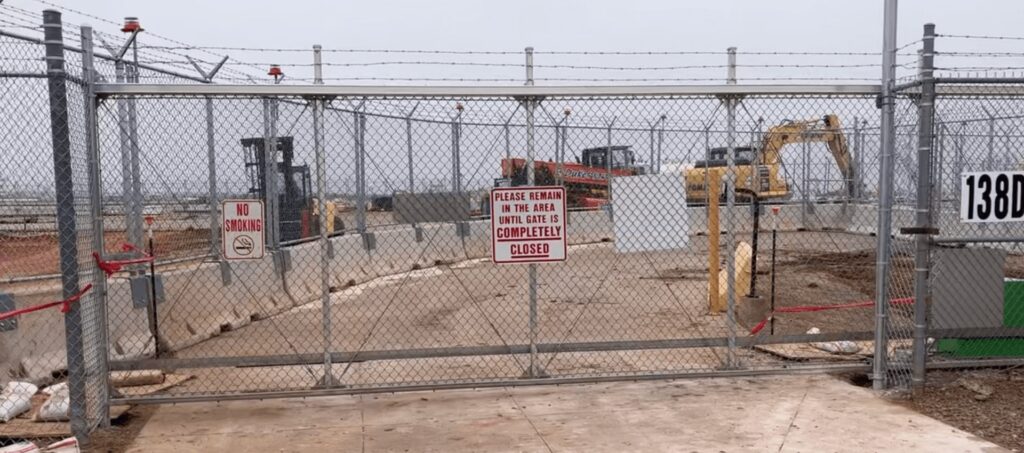 High-security chain-link gate with barbed wire and controlled access on construction site.