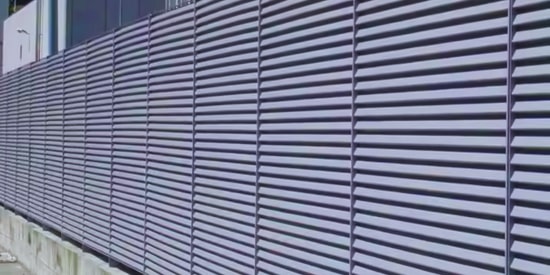 Louvered security fence providing privacy and airflow for a protected facility.