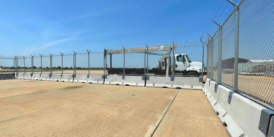 Temporary security fence with barbed wire and concrete barriers at a protected site.